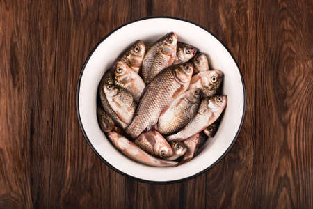 Catch of fishing. Full bowl of crucian carp on a brown wooden backgroundの写真素材