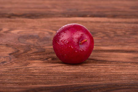 Fresh red plums with drops on a brown wooden backgroundの写真素材