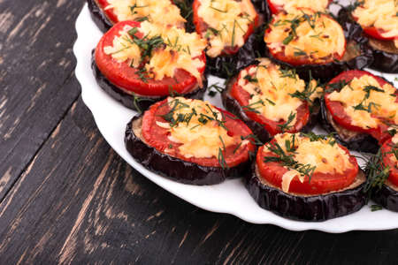 Dish of fried slices of eggplant, tomatoes and sprinkle with cheese and dill in a bowl on a wooden background closeupの写真素材