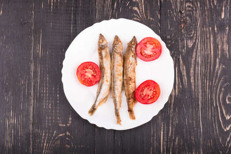 Grilled fish capelin on a plate with tomatoes on a wooden backgroundの写真素材
