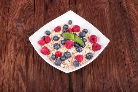 White bowl full of oatmeal with raspberries, blueberries and mint leaves on a wooden table