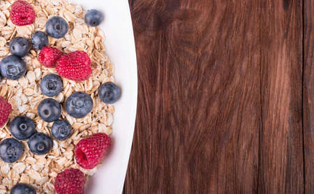 Part bowls filled with oatmeal and raspberries and blueberries on a wooden backgroundの写真素材