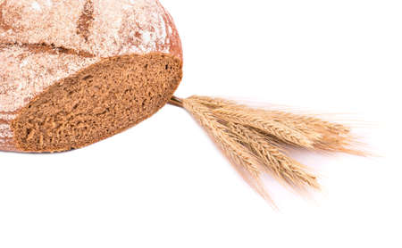 Cut homemade brown bread with spikelets of wheat on a white backgroundの写真素材
