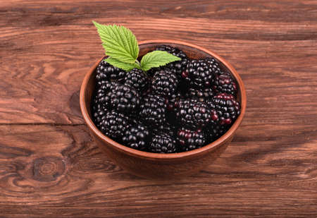 Plate full of fresh blackberries with leaves on a brown wooden tableの写真素材