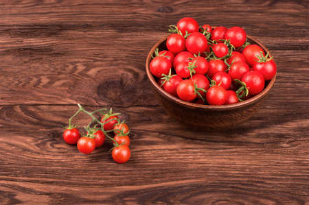 Full bowl of fresh small red cherry tomatoes with drops on a wooden tableの写真素材
