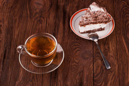 A cup of black tea with chocolate cake with cream on a wooden backgroundの写真素材