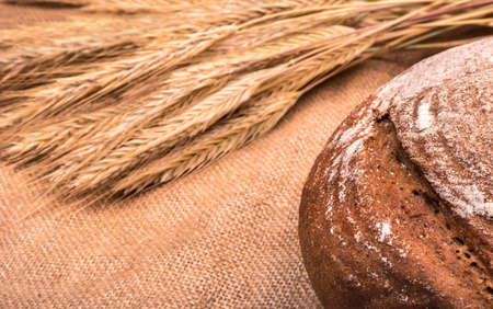 Homemade brown bread and wheat ears on sackcloth closeupの写真素材