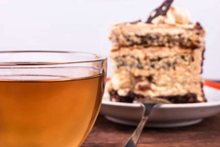 Glass cup of herbal tea and a slice of cake with chocolate and cream on the tableの写真素材