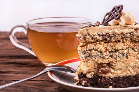 Piece of cake with chocolate and cream on a plate with a cup of herbal tea on a table close-upの写真素材