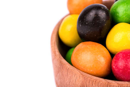 A pile of multi-colored candies in chocolate peanuts in a wooden bowl closeup