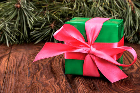 Christmas gift in a green box with a ribbon on a background of pineの写真素材