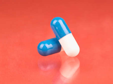Two blue and white capsules crossed on peachy background