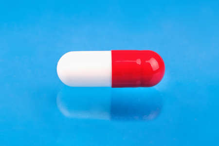 Single red white capsule close-up on a blue backgroundの写真素材