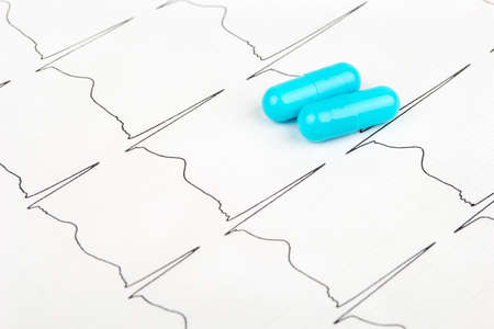 Cardiogram with the rhythm of the heartbeat and the two blue capsules closeupの写真素材