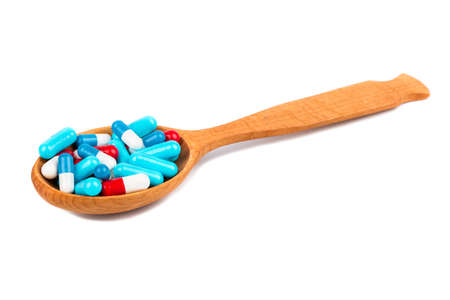 Wooden spoon filled with multicolored capsules on white backgroundの写真素材