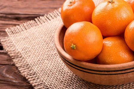 Wooden bowl filled with fruit mandarins on a napkin sackcloth closeupの写真素材