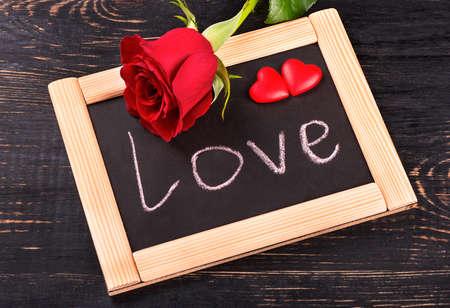 Board with the word love, red rose and hearts symbolizing valentines dayの写真素材