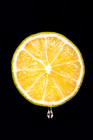 Half of fresh fruit with a drop of lime juice on a black backgroundの写真素材