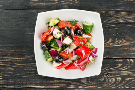 White bowl with fresh Greek salad on a dark table, top viewの写真素材