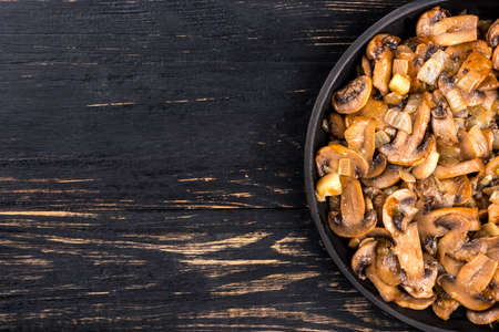 Part of the frying pan with fried mushrooms champignon on empty wooden backgroundの写真素材
