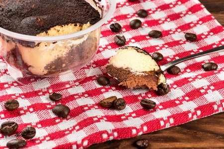 Piece of tiramisu in a spoon on a table with scattered grains of coffeeの写真素材