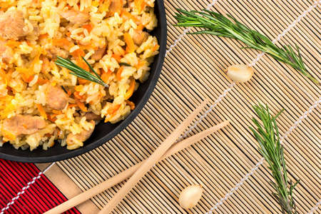 Part of the frying pan with cooked Asian pilaf on bamboo napkin with spices and chopstick top viewの写真素材
