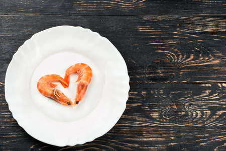 Boiled shrimp in a heart shape on the plate on a wooden backgroundの写真素材