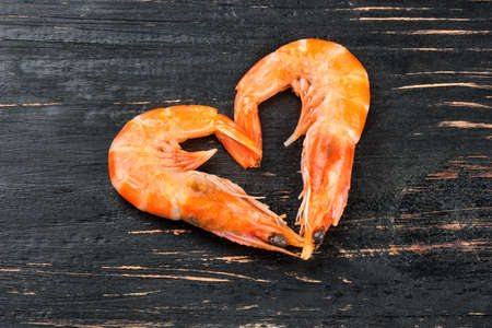 Two boiled shrimp in the shape of a heart on a dark wooden backgroundの写真素材