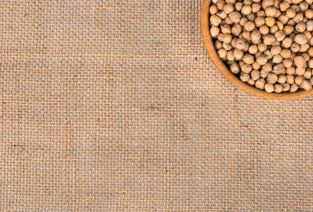 Part of a wooden bowl filled with dry chickpeas on an empty sackingの写真素材