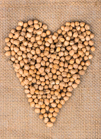Dry chickpeas in the shape of a heart on sackcloth, top view