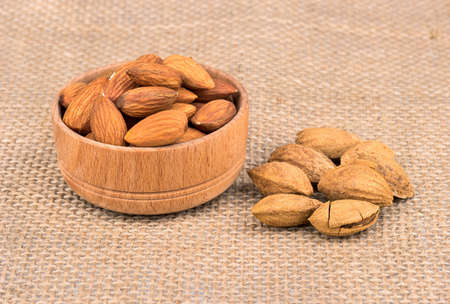 Filled with wooden bowl with dry almonds and walnuts in shell scattered on a sackcloth