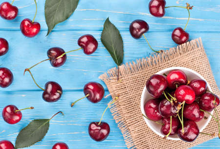 Full bowl sweet red cherries with scattered leaves and berries on a wooden background, top viewの写真素材