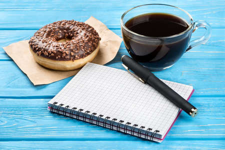 Chocolate donut with coffee and office notebook on the tableの写真素材