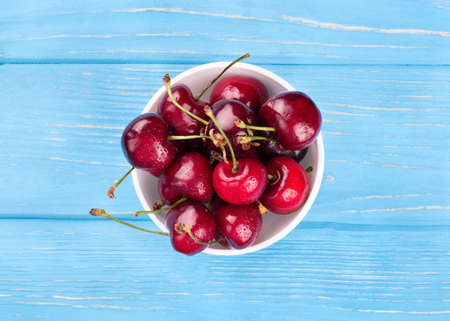 Bowl full of red cherries with drops on a blue table, top viewの写真素材