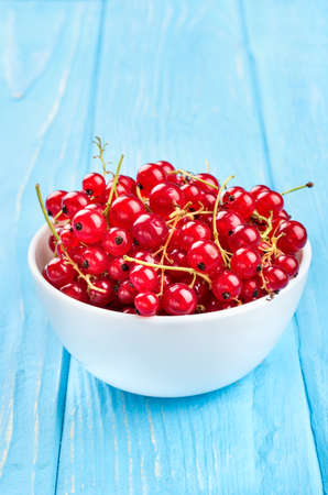 Ceramic white bowl with fresh berries currant on a blue table, close-upの写真素材