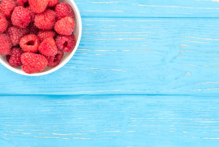 Part of the bowl with fresh red raspberries on an empty wooden table, top viewの写真素材