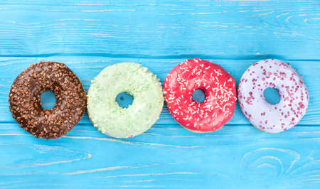 Four donut with multicolored glaze on a blue wooden background top viewの写真素材