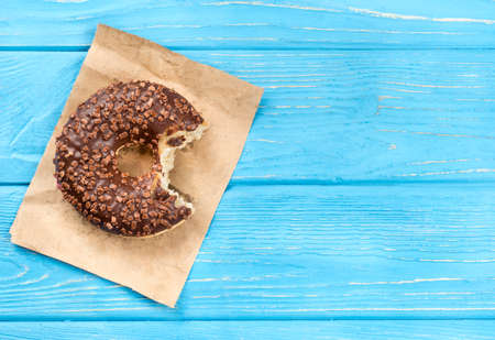 Bitten chocolate donut on paper and a blank wooden background, top viewの写真素材
