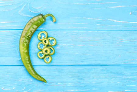 Fresh green chili pepper with slices on a blue wooden background, top viewの写真素材