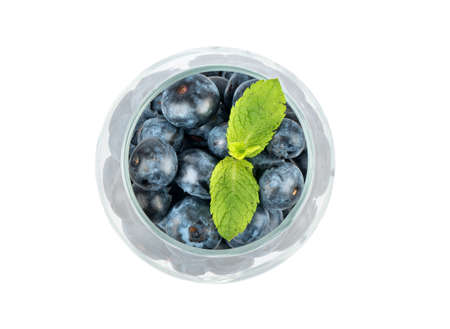 Ripe blueberries with mint leaves in a glass on a white background, top view