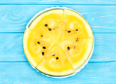 Four slices of yellow watermelon on a plate and table, top view