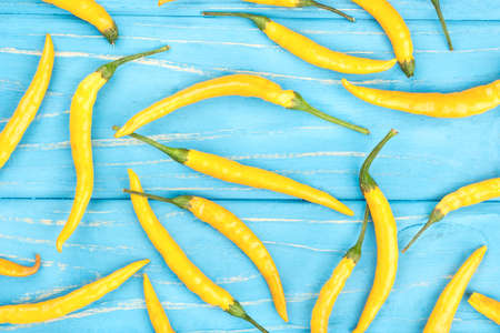 Scattered yellow chili peppers on a wooden background, top view