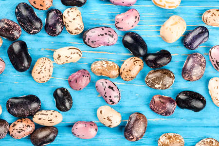 Diffuse dry colored kidney bean on a wooden background, top view