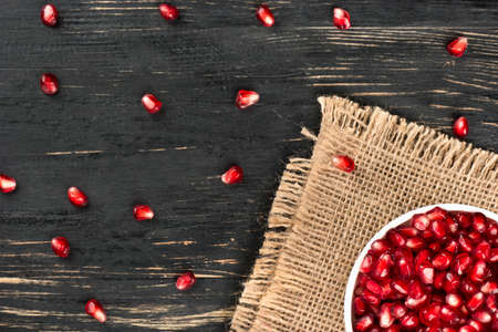Part of the bowl with pomegranate seeds on sackcloth and table, top viewの写真素材