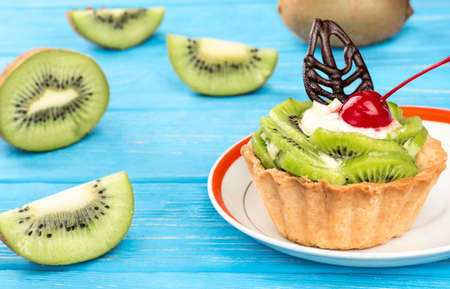 Delicious fruit cake with kiwi on a plate and fruit scattered on a blue tableの写真素材