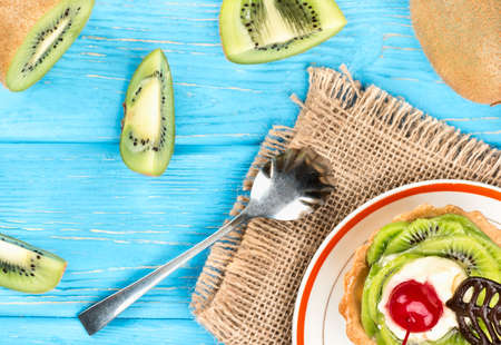 Delicious tart with kiwi on a plate, and sackcloth with scattered fruit, top viewの写真素材