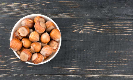 White ceramic bowl full of hazelnuts in the shell on a blank wooden background, top viewの写真素材