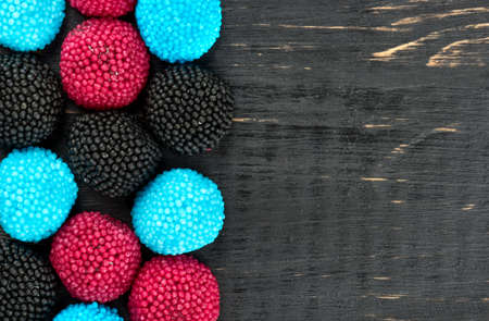 Scattered colored berry jelly candies on a blank wooden background, top view