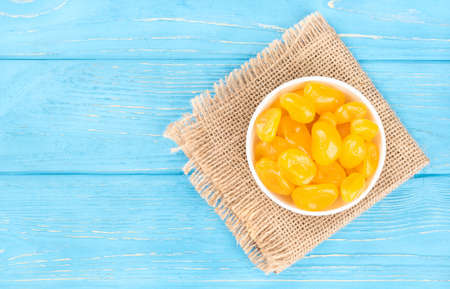 White bowl of dried yellow kumquat on the sacking and an empty wooden background, top viewの写真素材