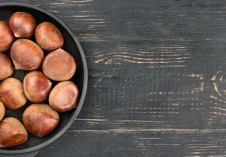 Part of the frying pan with fresh chestnuts on an empty wooden background, top viewの写真素材